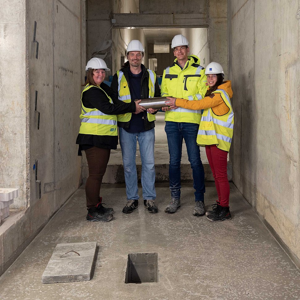 Prof. Kristian Franze, Dr. Dorothe Burggraf, Adrian Thoma and Katharina Kißner are gathered around the MPZPM time capsule before it is lowered into the concrete.